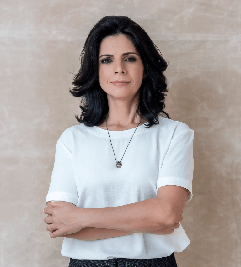 Advogada Alexandra Elgui em pé e com braços cruzados, ela veste uma blusa branca, um colar preto uma calça social preta